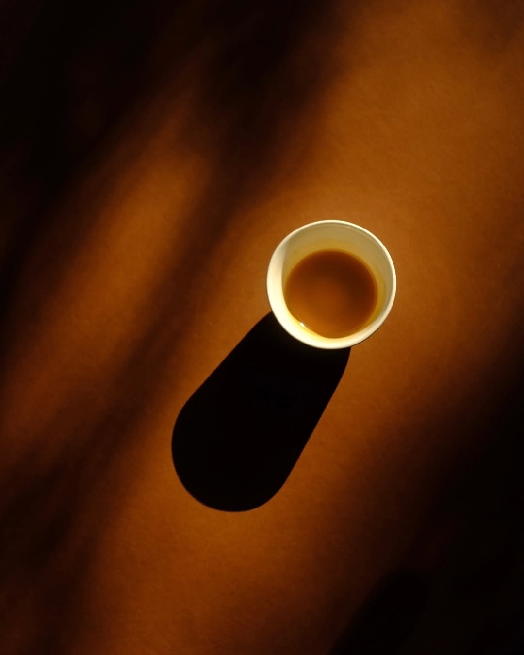 A cup of coffee casting a long shadow in warm sunlight.